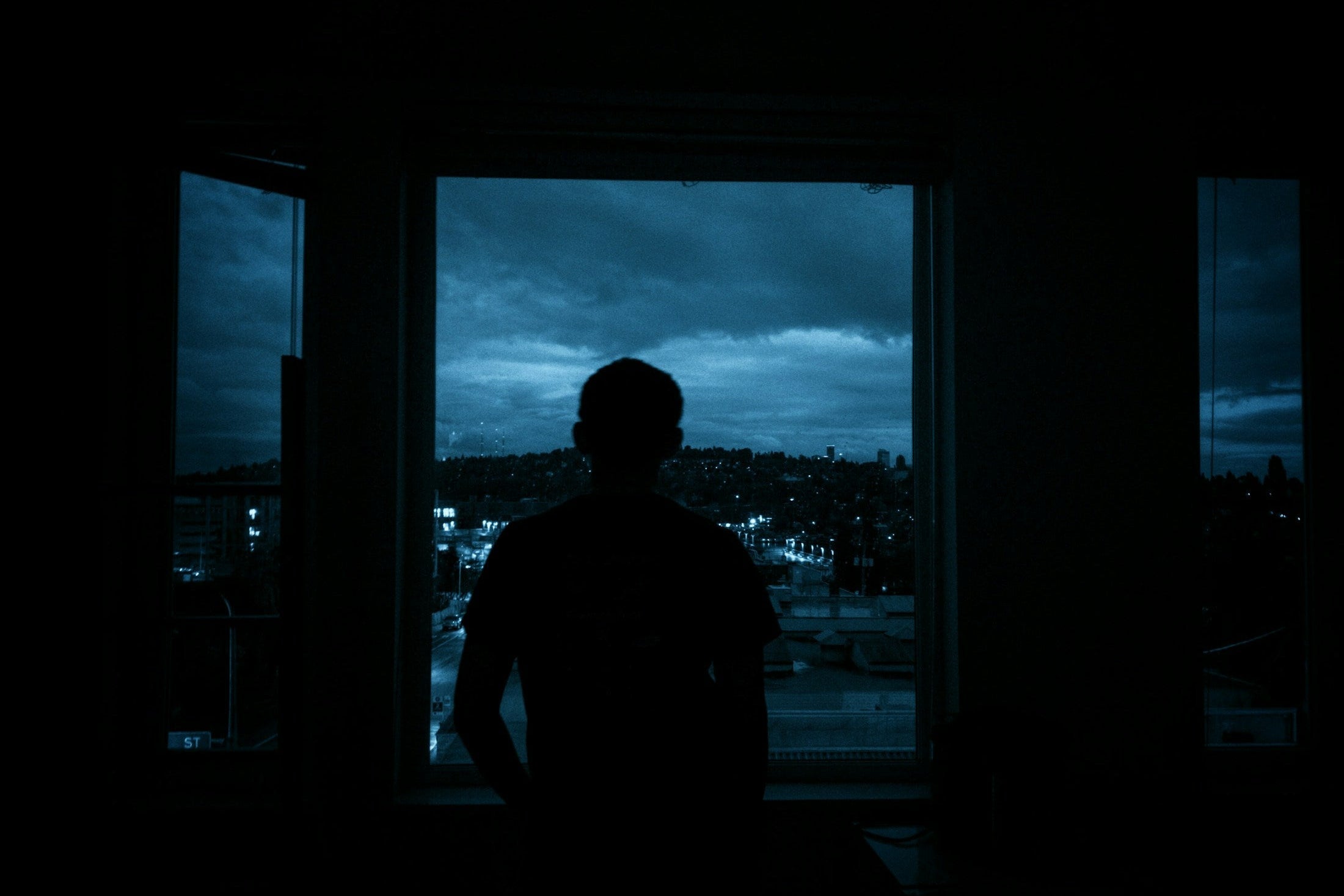 Man looking out of a window at a city at night, alone with his thoughts