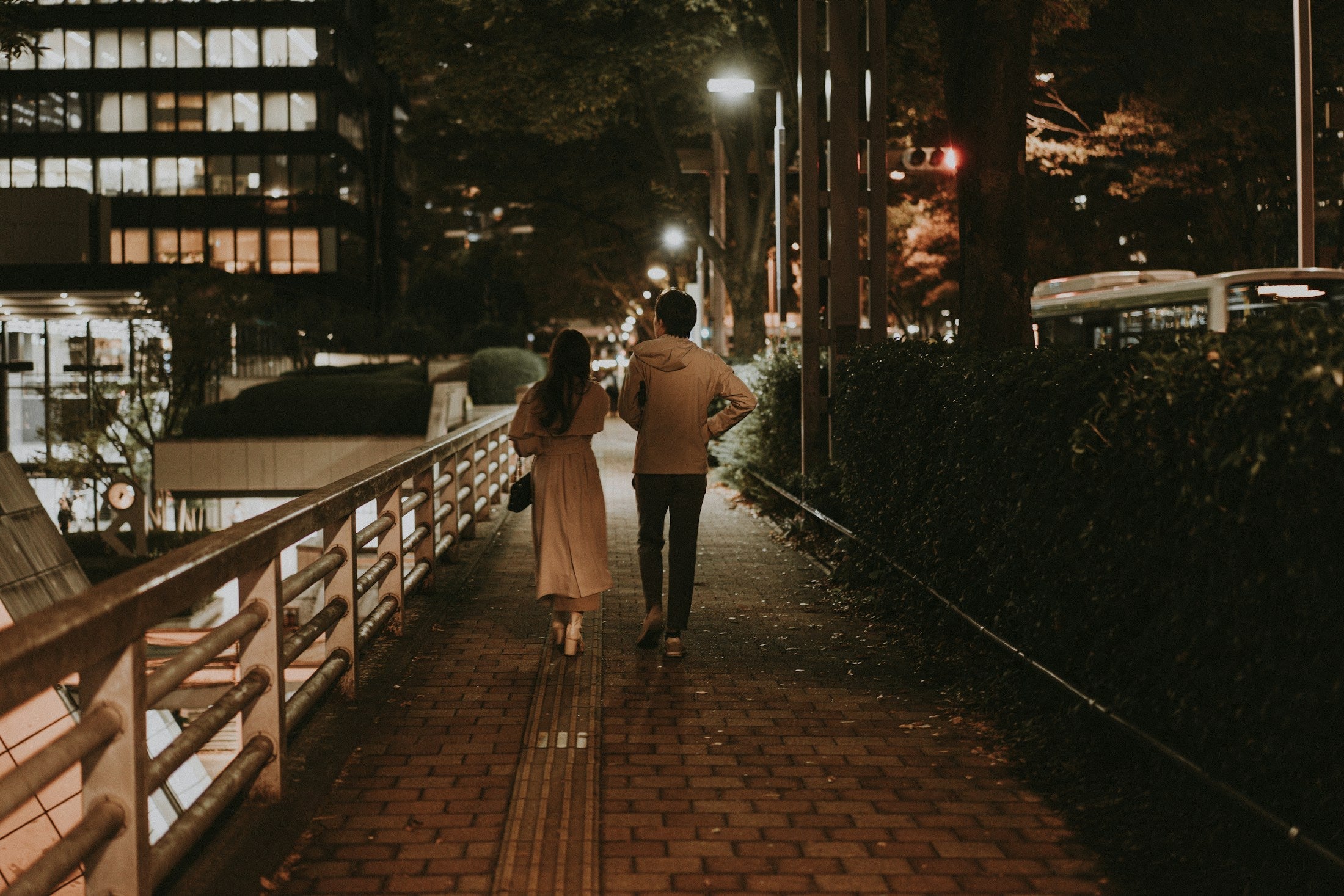 Two people walking a city pavement together at night under street light