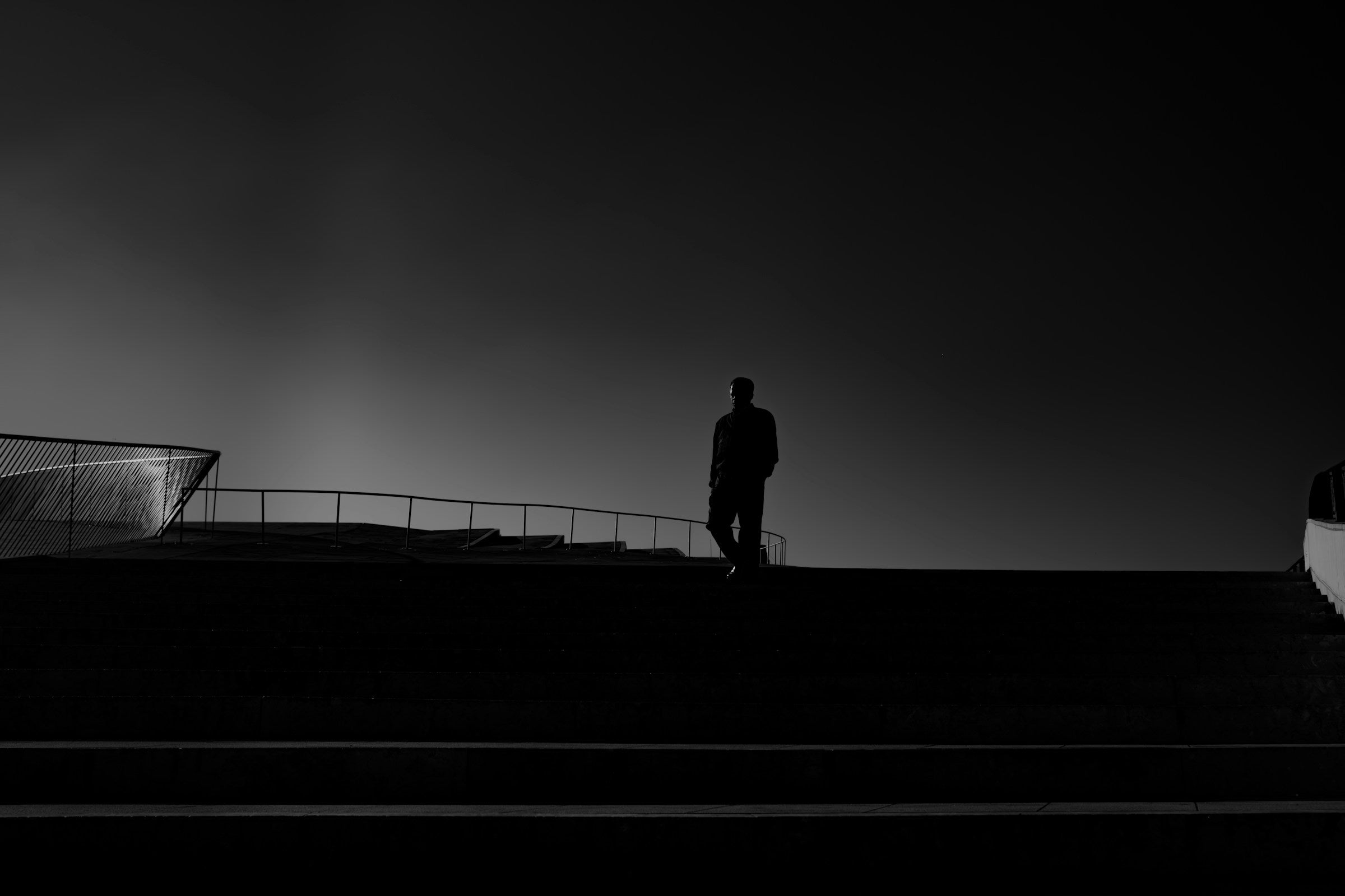 Black and white silhouette of a man standing alone on an elevated walkway against a dark sky