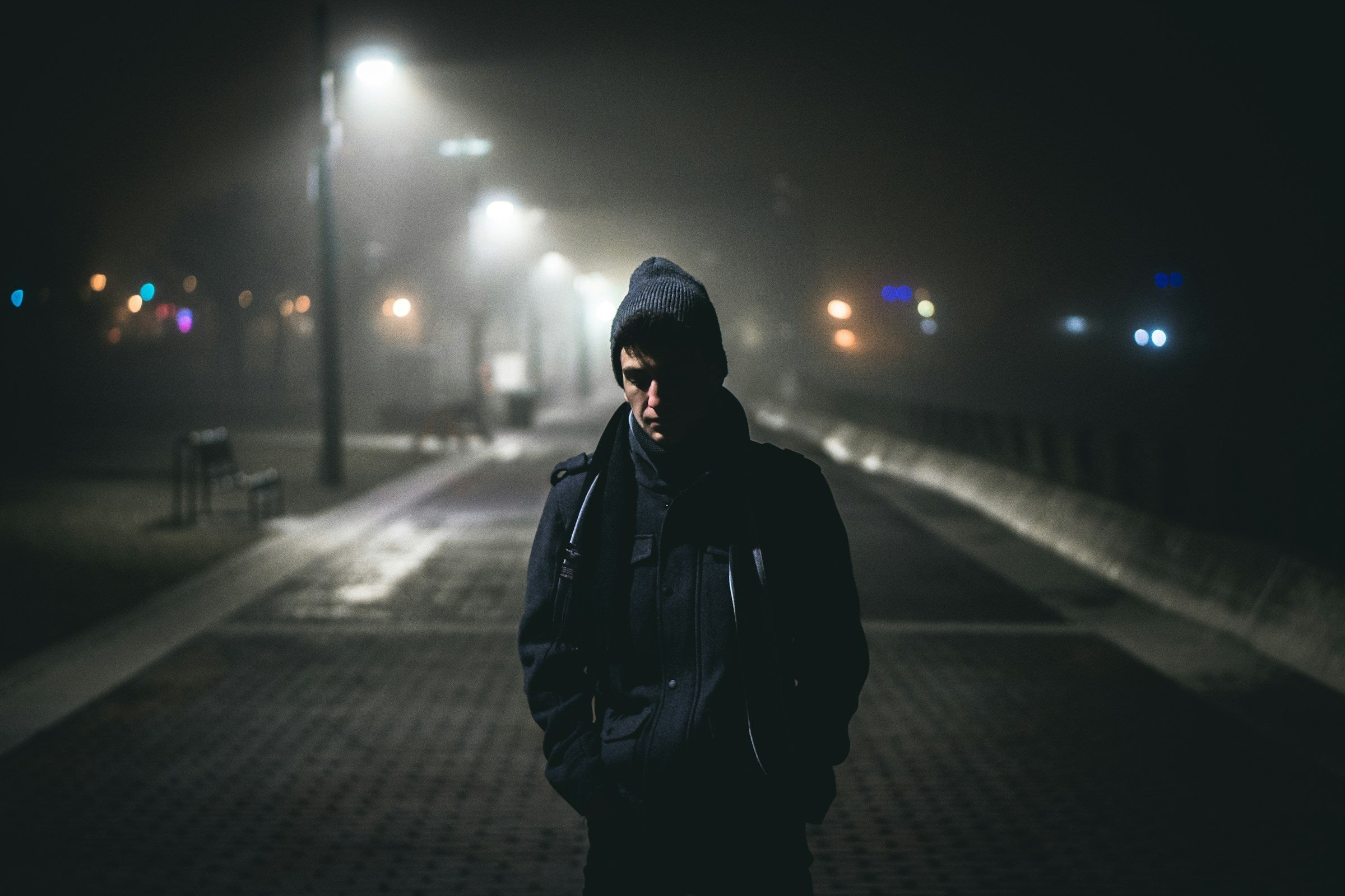 Lone figure in a hooded coat standing on an empty mist-lit street at night