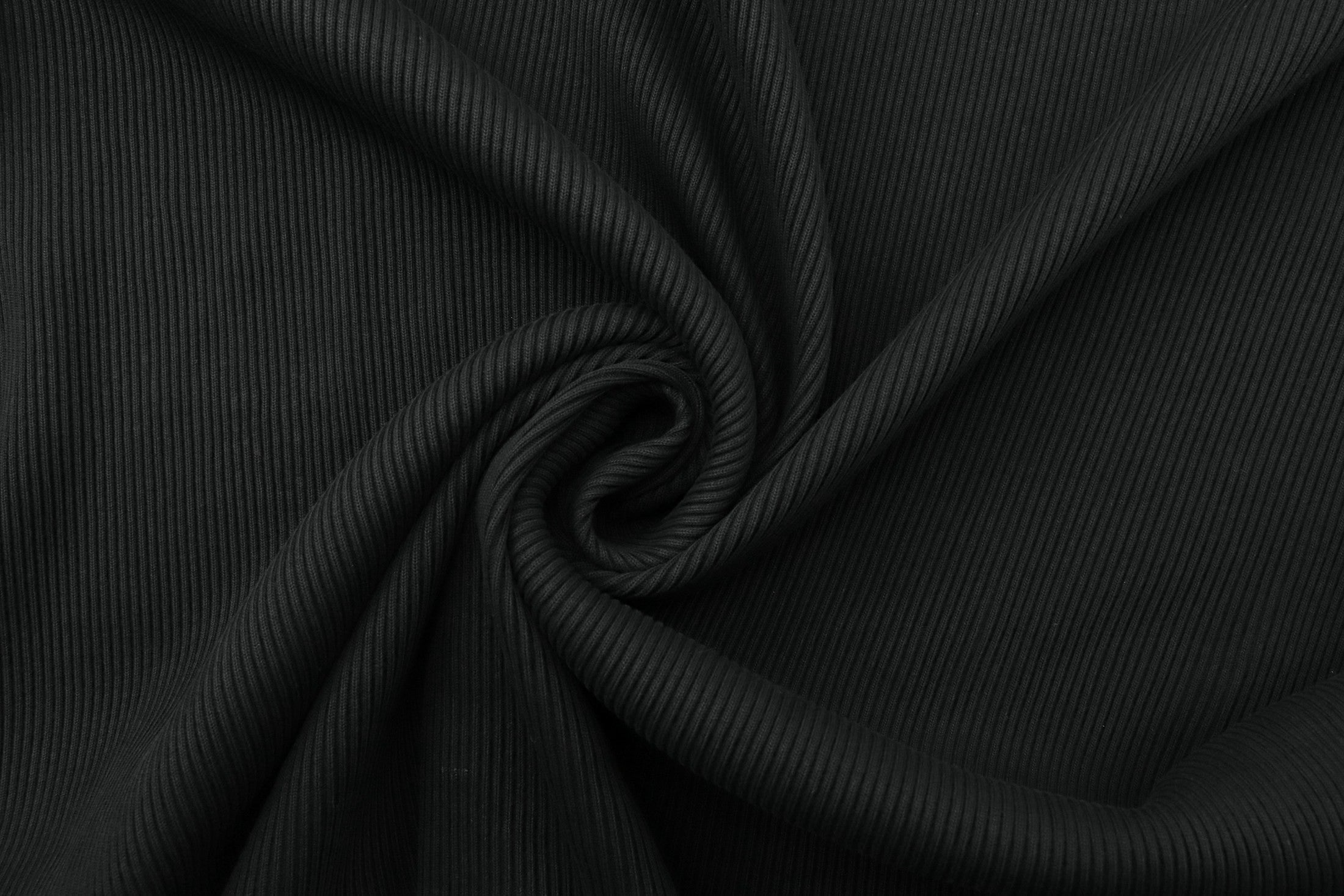 Close-up of black ribbed cotton drawn into a spiral fold, showing the rib and the drape