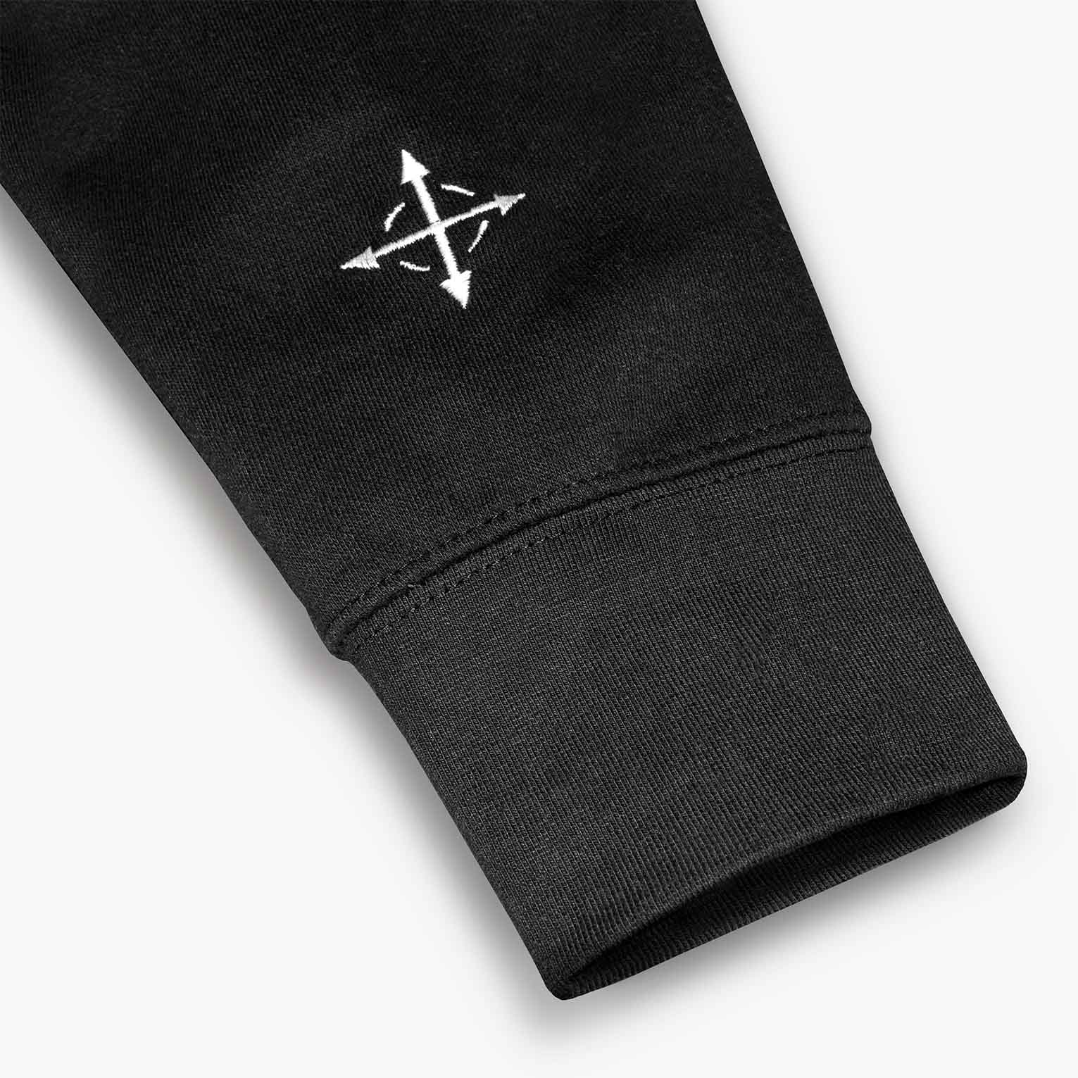 Embroidered compass mark on the sleeve of the SAINTS WORLDWIDE black hoodie, above the ribbed cuff