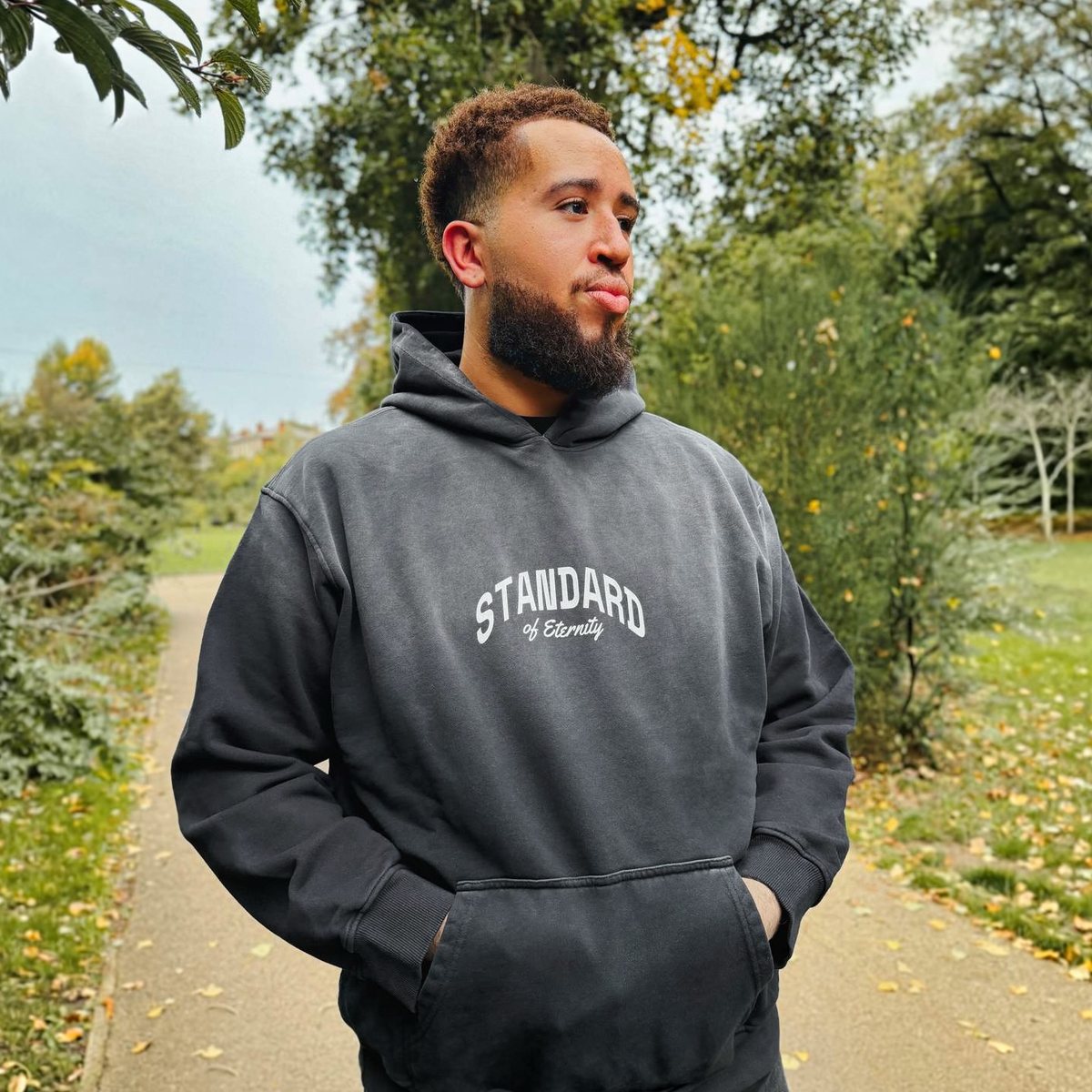 Man wearing the STANDARD Hoodie in washed black, front view, STANDARD of Eternity arched across the chest